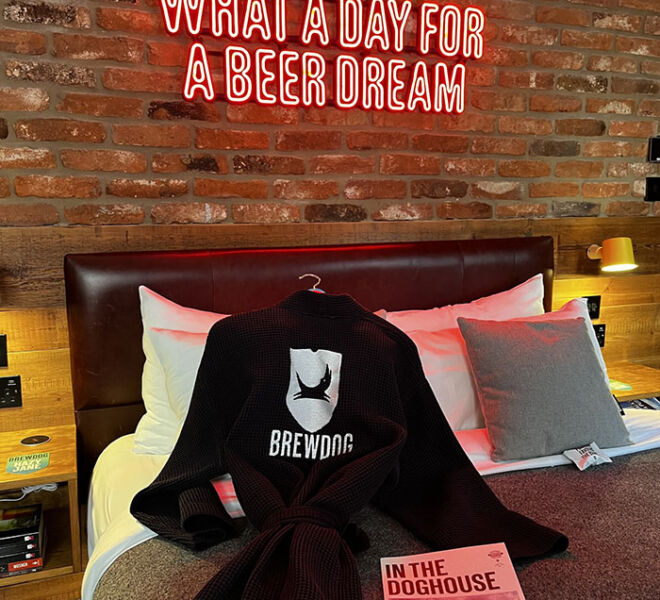 Bed in Doghouse hotel with lighted sign and robe on bed