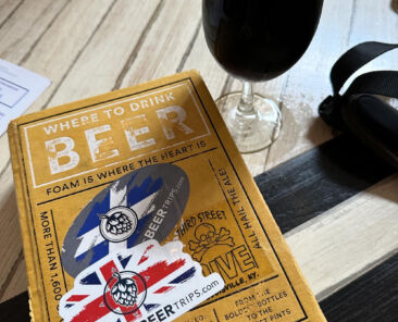 beer book with epic beer trip stickers next to pint of dark beer